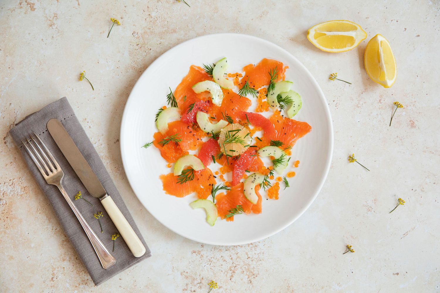 Fresh salmon salad with greens and citrus garnish served on white plate with cutlery from a product photoshoot.