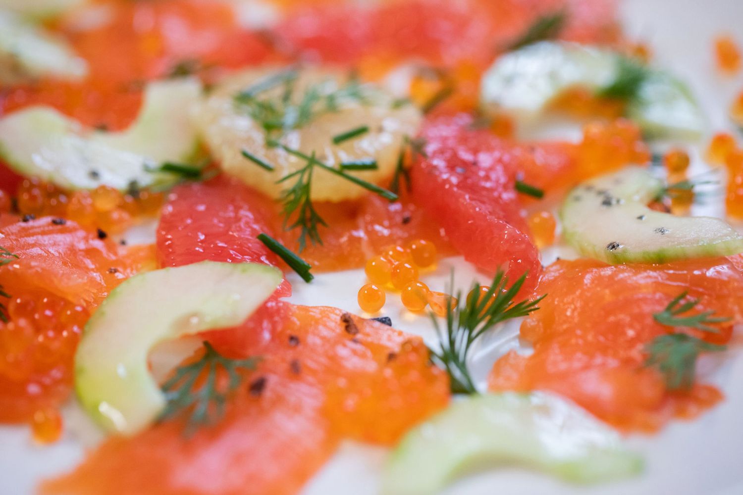 Fresh salmon carpaccio garnished with cucumber slices, dill, and black pepper on a white plate from a product photoshoot.
