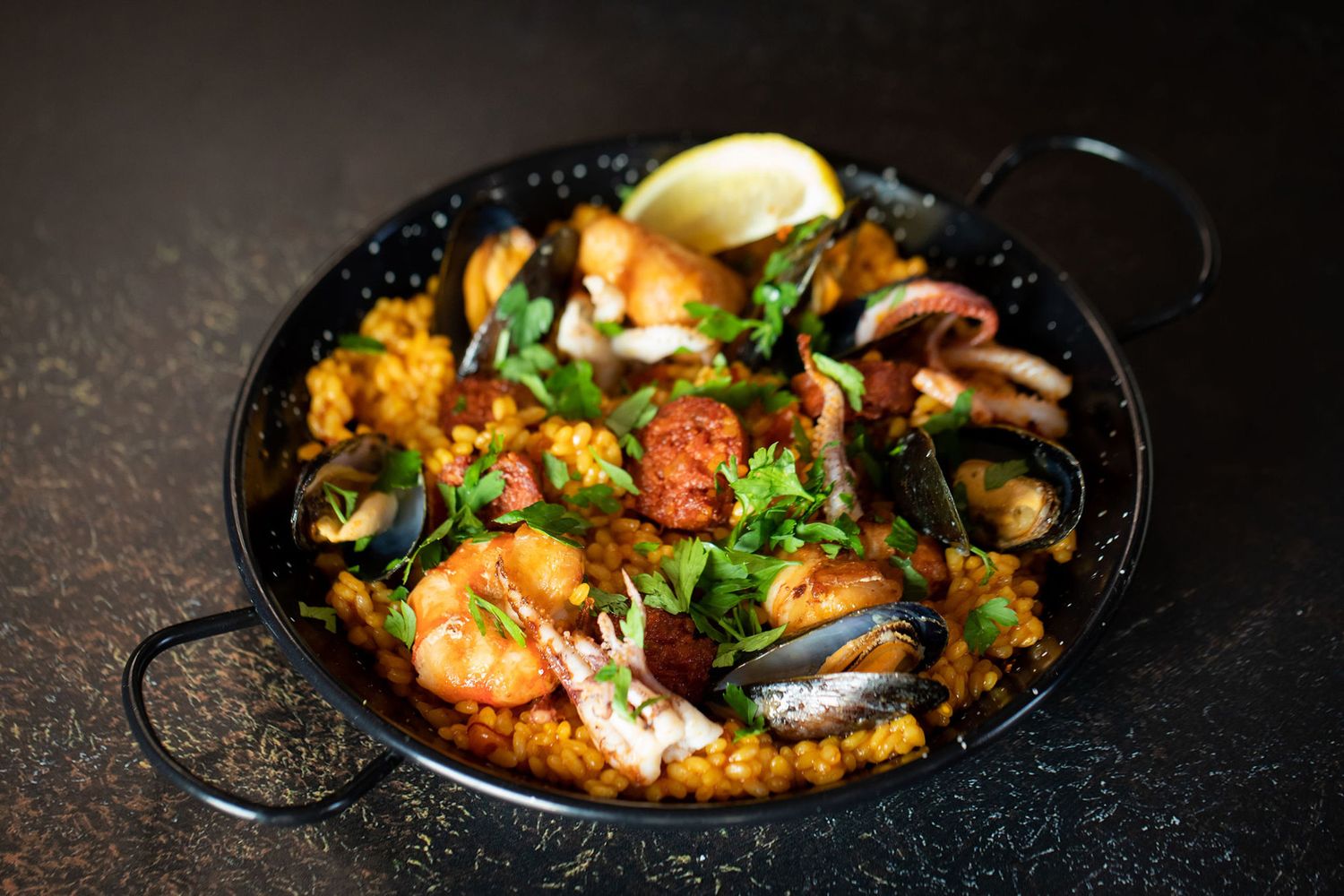 Seafood paella with shrimp, mussels, and herbs in a traditional black pan from a product photoshoot.