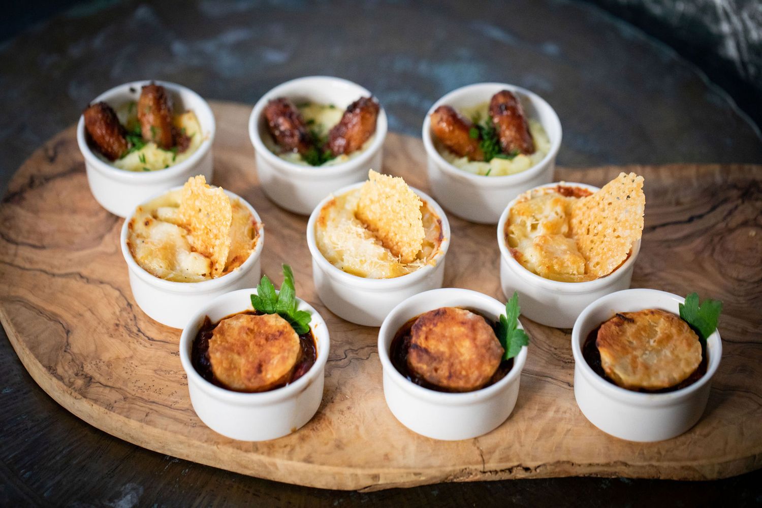 Small appetizers served in white ceramic bowls arranged on a wooden board from a product photoshoot.