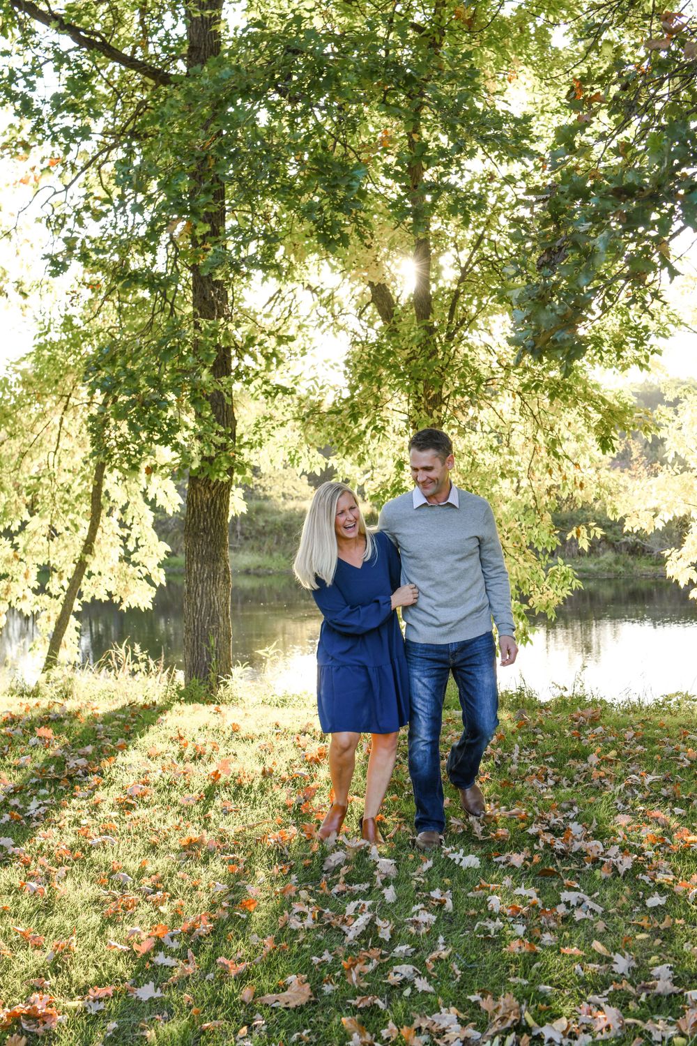 Family walking together through autumn leaves by riverside.