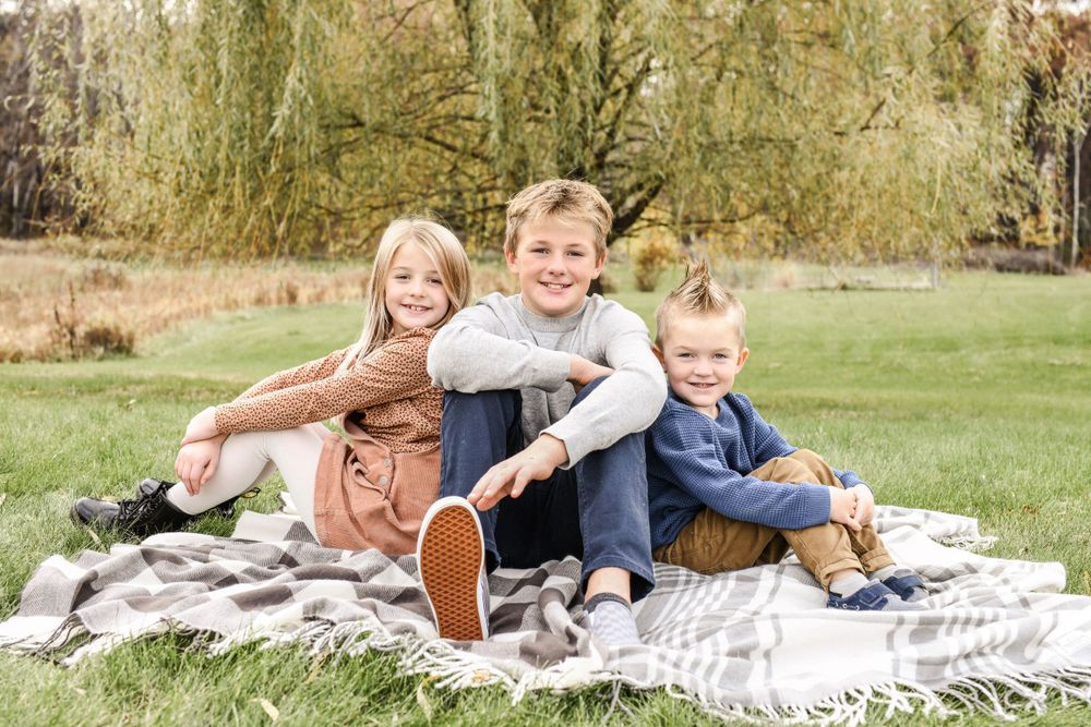 Family relaxing together on a picnic blanket under a willow tree.