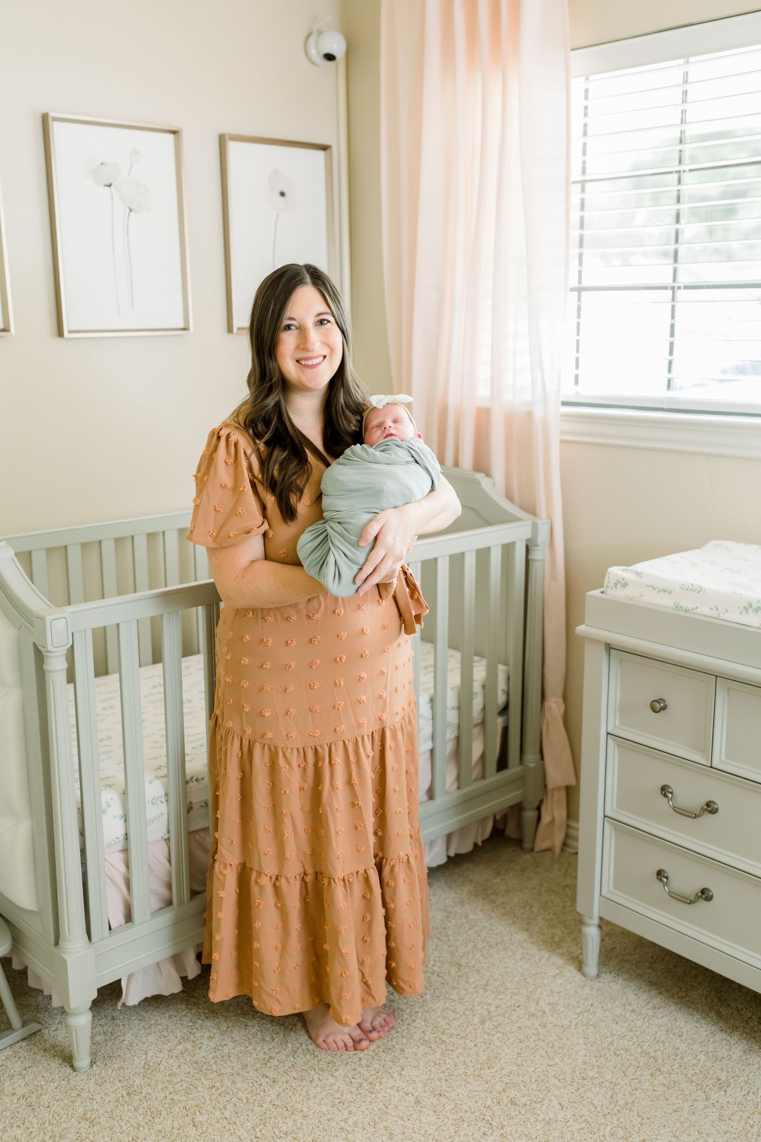 A tender nursery moment featuring a peach-colored dress and soft gray crib in a delicately decorated room.