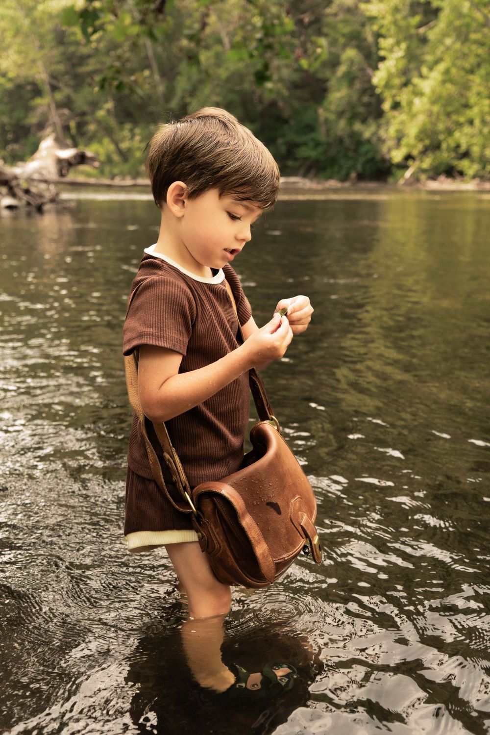 boy stands in river examining shell