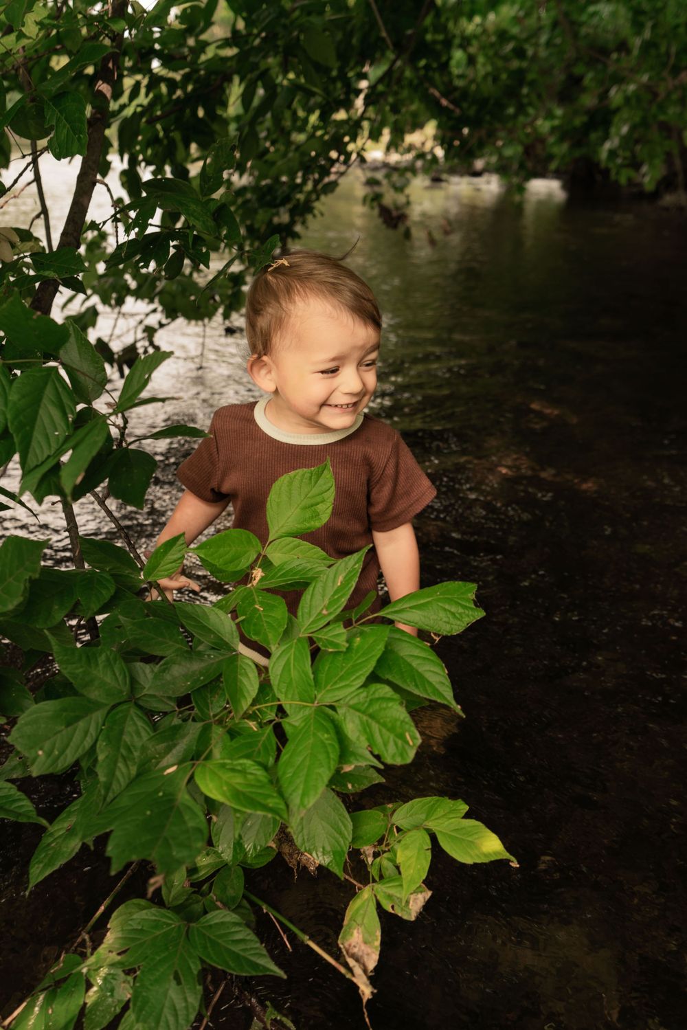 toddler boy smiles standing in river