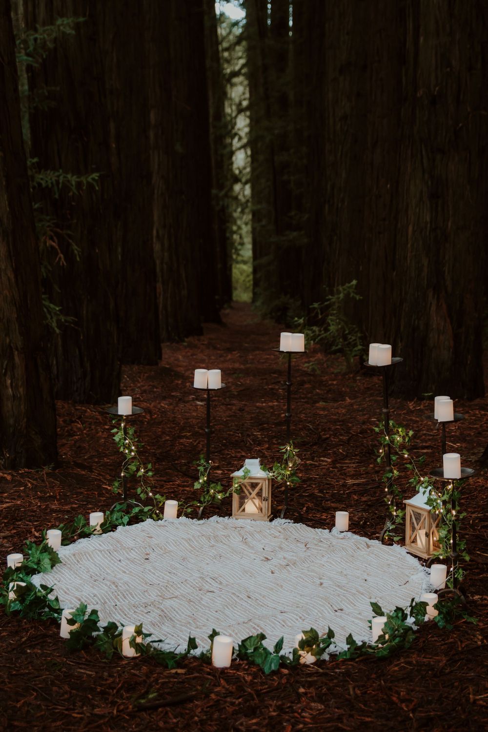 Forest wedding setup with white lanterns and greenery arranged in a circular pattern.