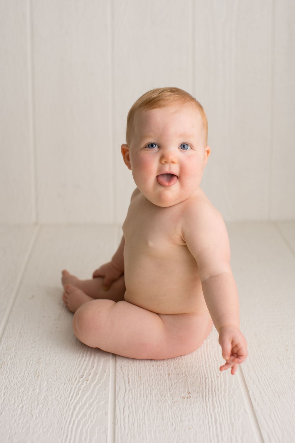 A delighted baby sitting on white wooden floor during portrait session.