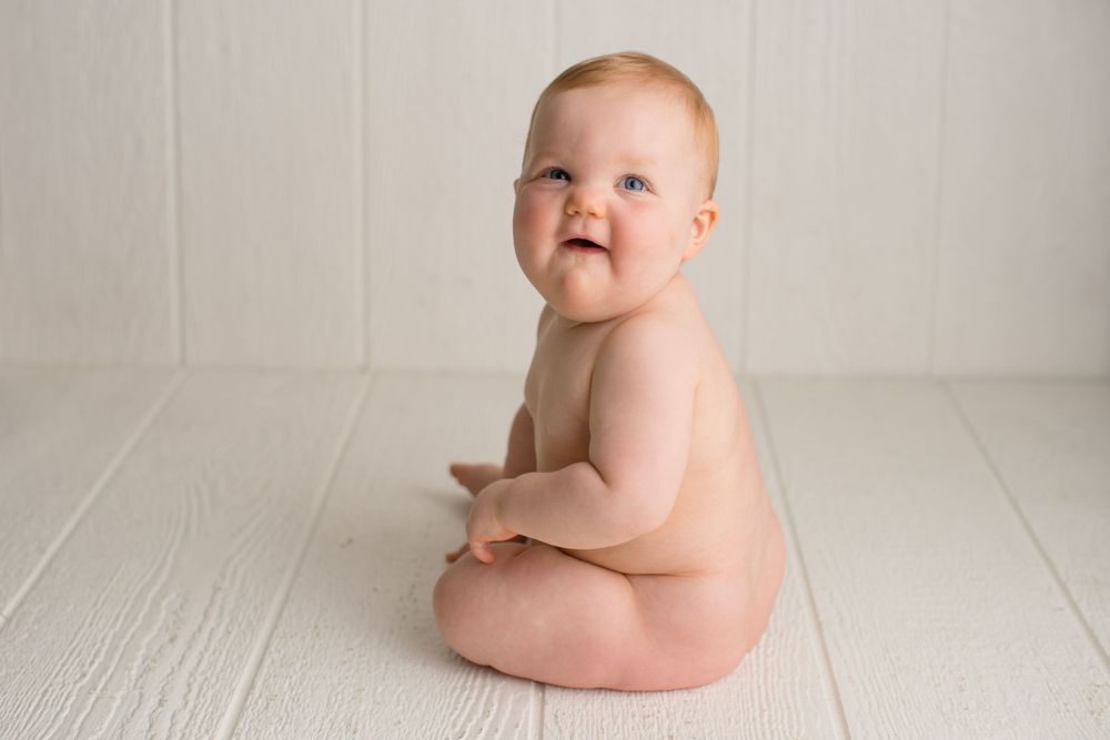A smiling baby sitting on white wooden floor during portrait photography.