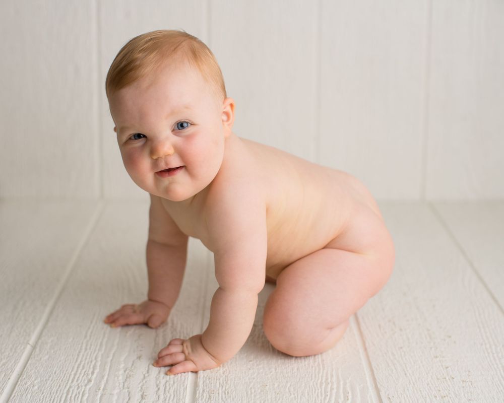 A crawling baby on white wooden floor during minimalist photography session.
