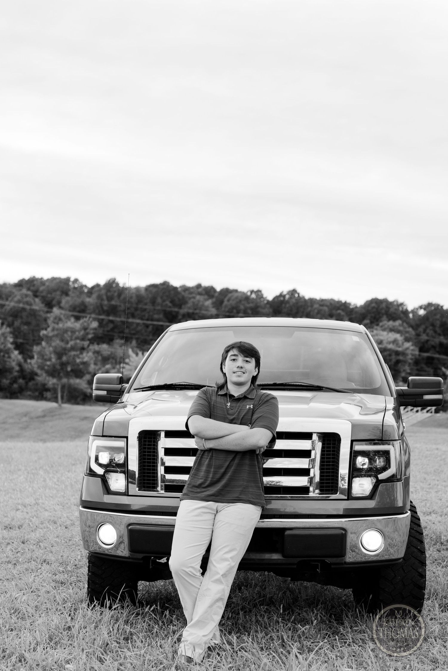 A black and white photo of someone leaning against the front of a Ford pickup truck.