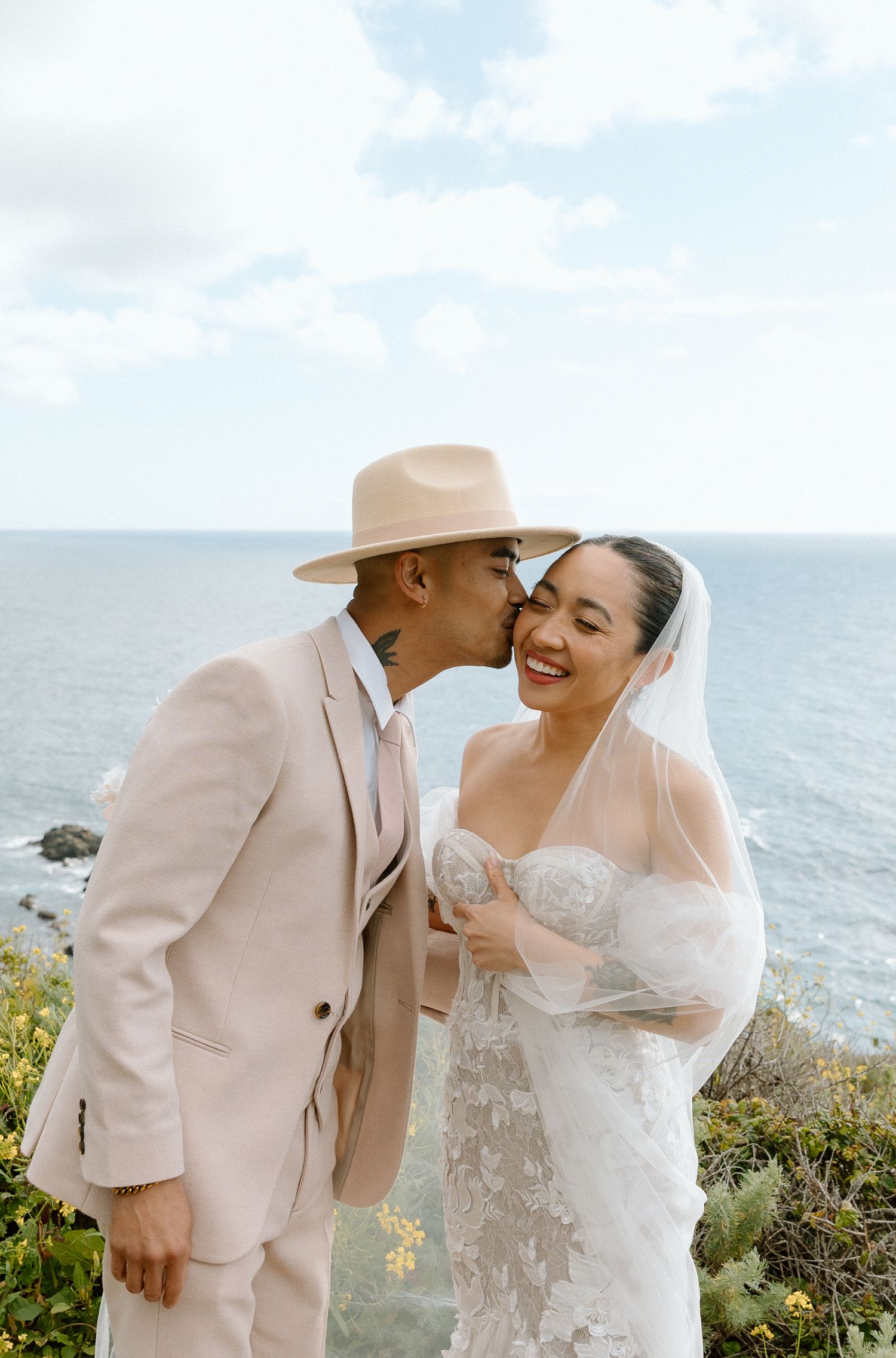 Joyful seaside wedding portrait with couple laughing against ocean backdrop.