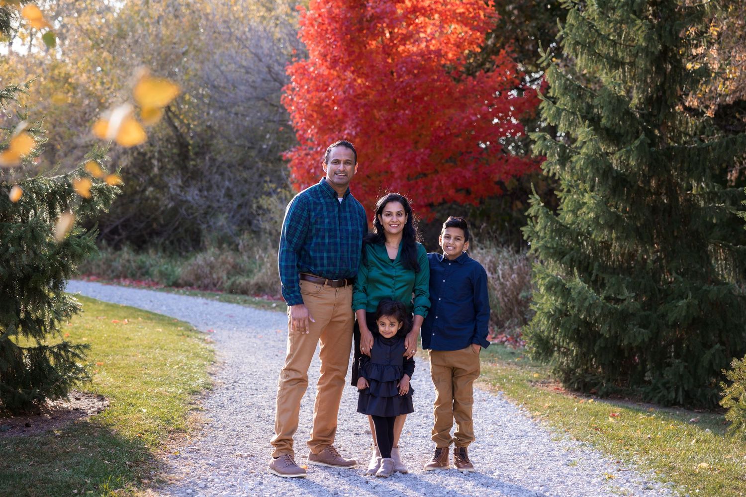 Family of four standing on path with vibrant red maple tree in autumn setting.