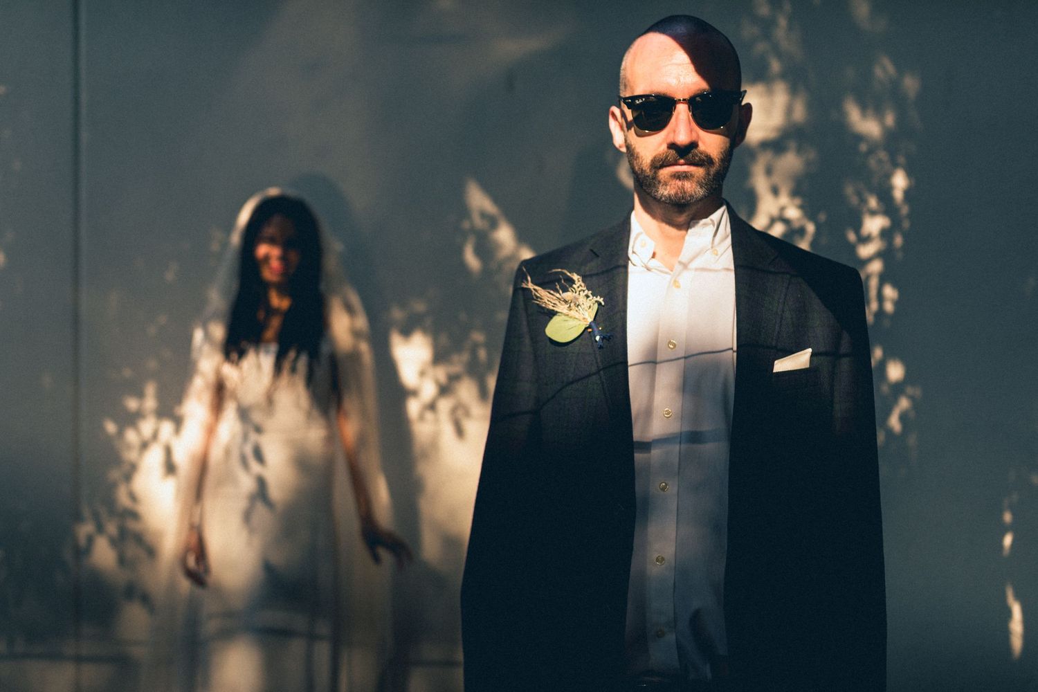 Artistic wedding photo with dramatic shadows and silhouette of a person in white dress in the background.