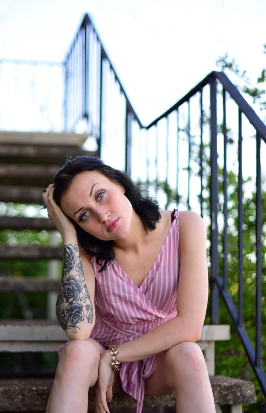 Person in striped dress sitting on outdoor stairs with metal railing.