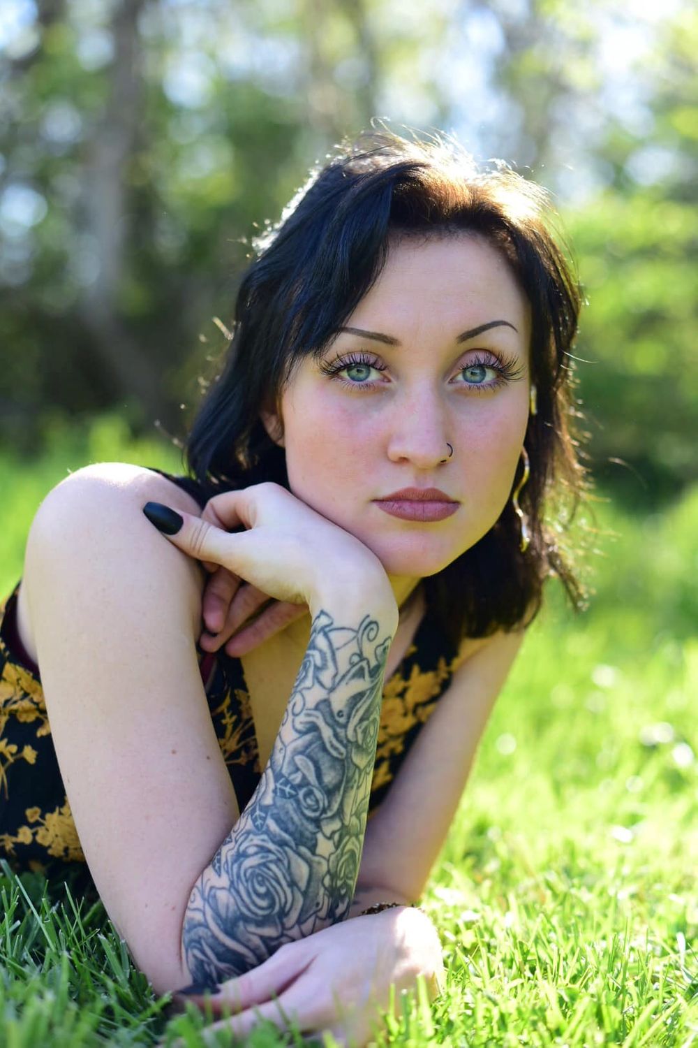 Portrait showing tattooed arm while posing in sunny grass field.