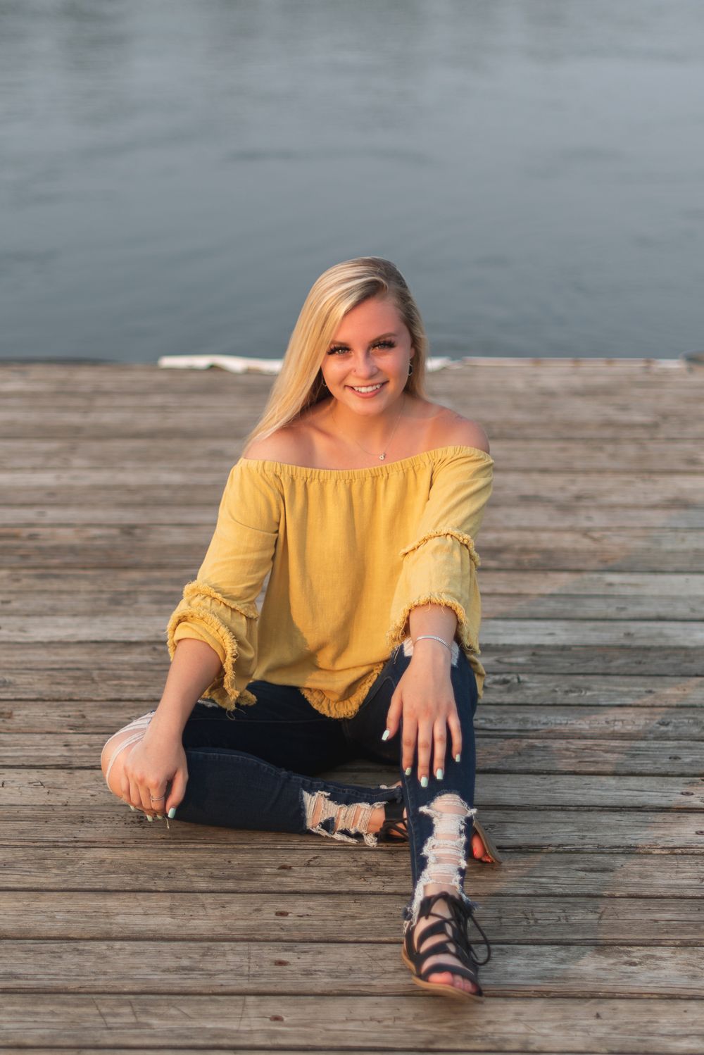 Portrait session on wooden dock by water wearing yellow top and distressed denim.