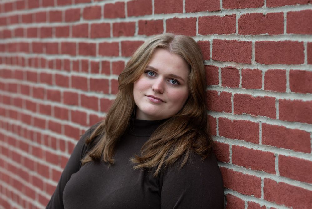 Portrait against red brick wall wearing dark turtleneck.