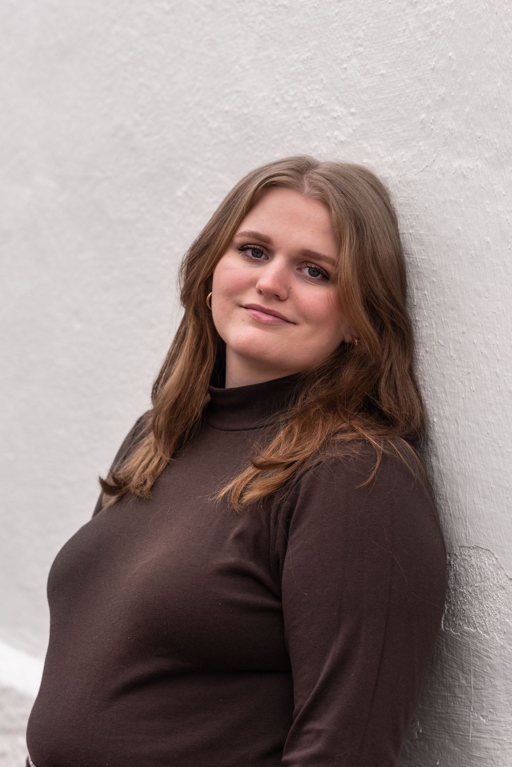 Portrait against white wall in brown turtleneck sweater.