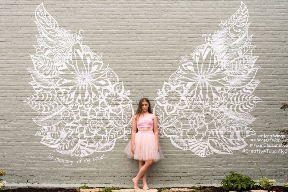 Artistic wall photos with decorative white angel wing murals painted on grey background.