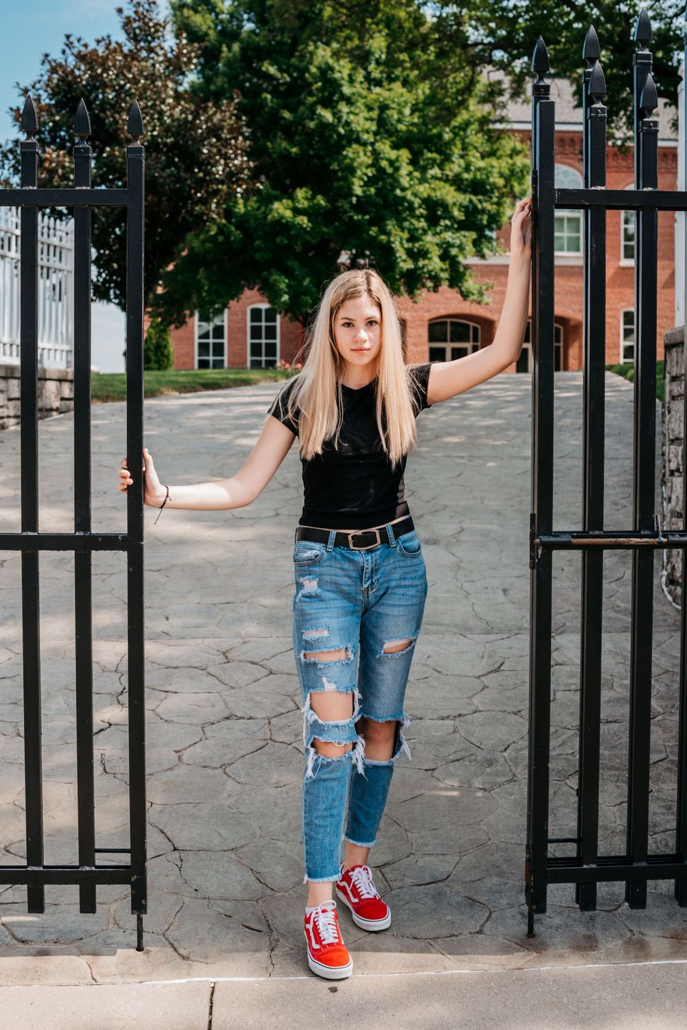 Distressed blue jeans and red sneakers shown near black metal gate in casual street style series.