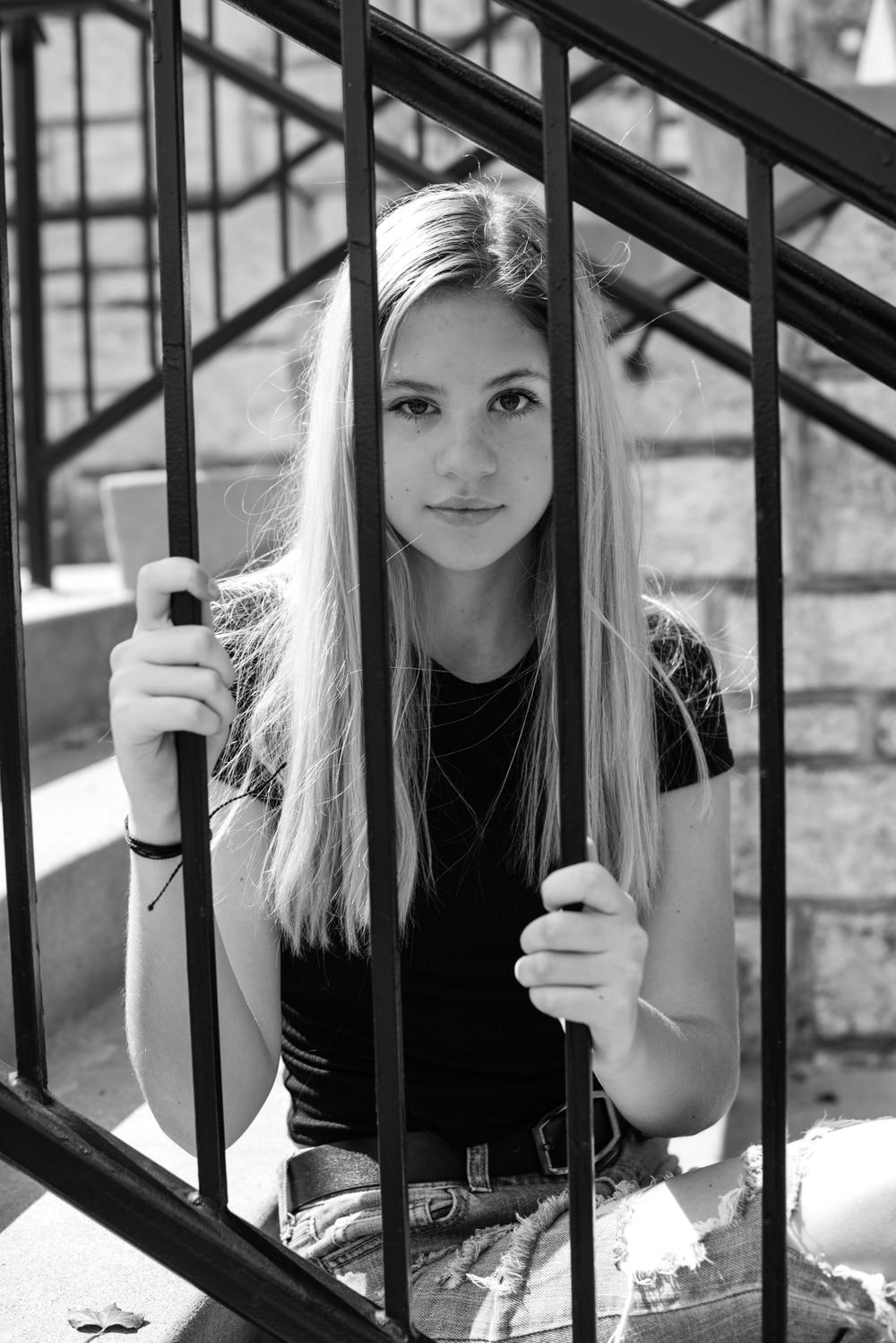 Artistic portrait series through black metal railings in natural sunlight.