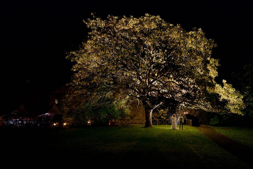 Bride & Groom under backlit tree at Holne Park House in Devon. Creative nightime portrait by Passion 4 Photos.