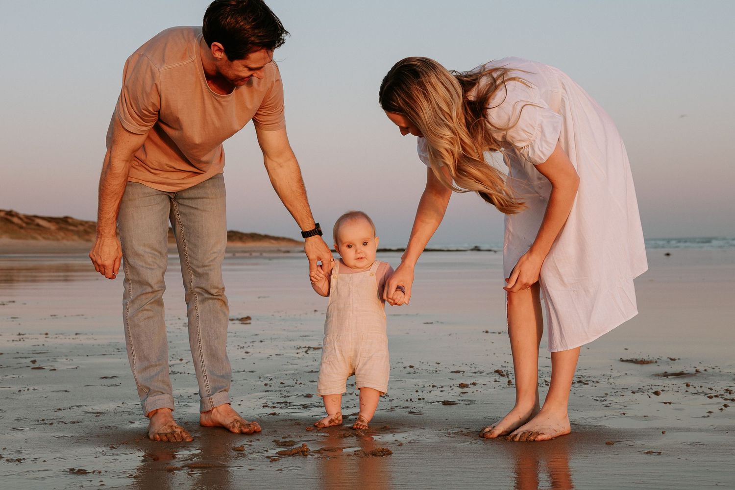 A family enjoying a tender moment together on a sandy beach at sunset.