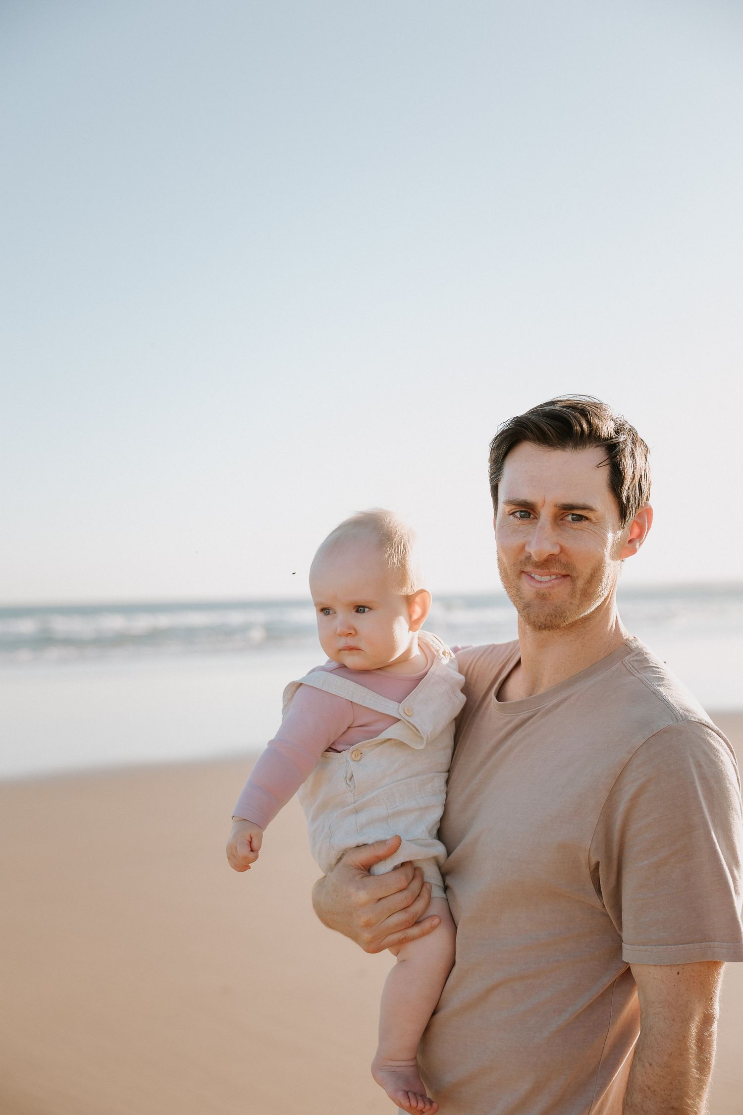 Father and baby enjoying sunny day at beach.