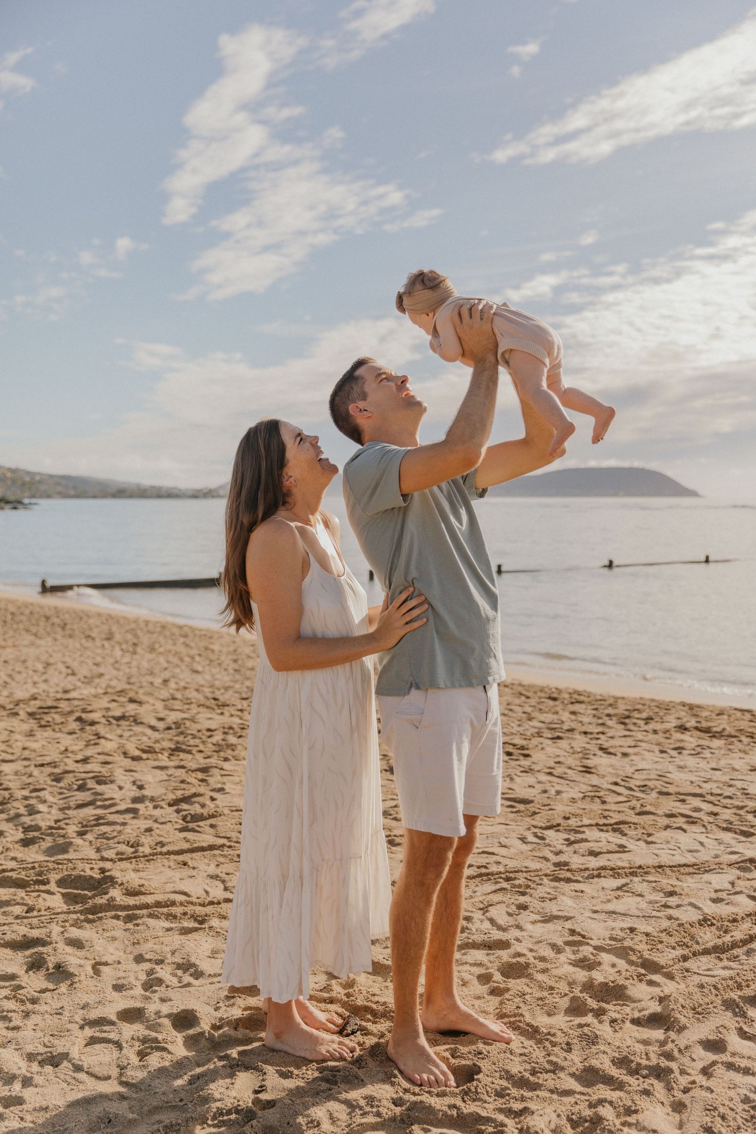 Family enjoying a sunset moment together on a sandy beach with ocean and cloudy sky in the background.
