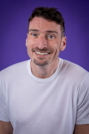 Comedian Alex Howard against a purple background shot in studio in Amy Davies Photography studio in Hove