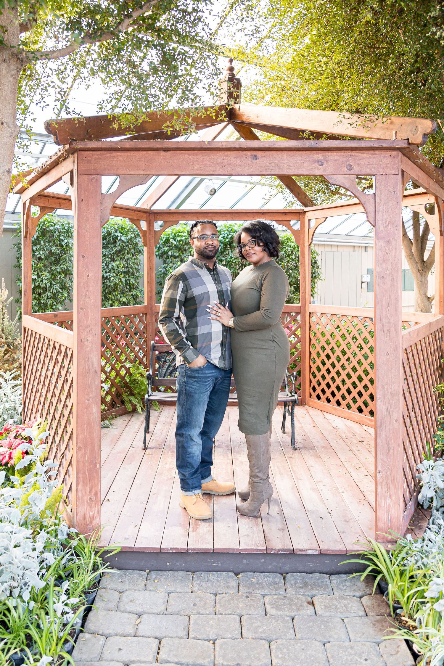 Couple sharing a romantic moment under a wooden garden gazebo surrounded by blooming flowers and greenery.