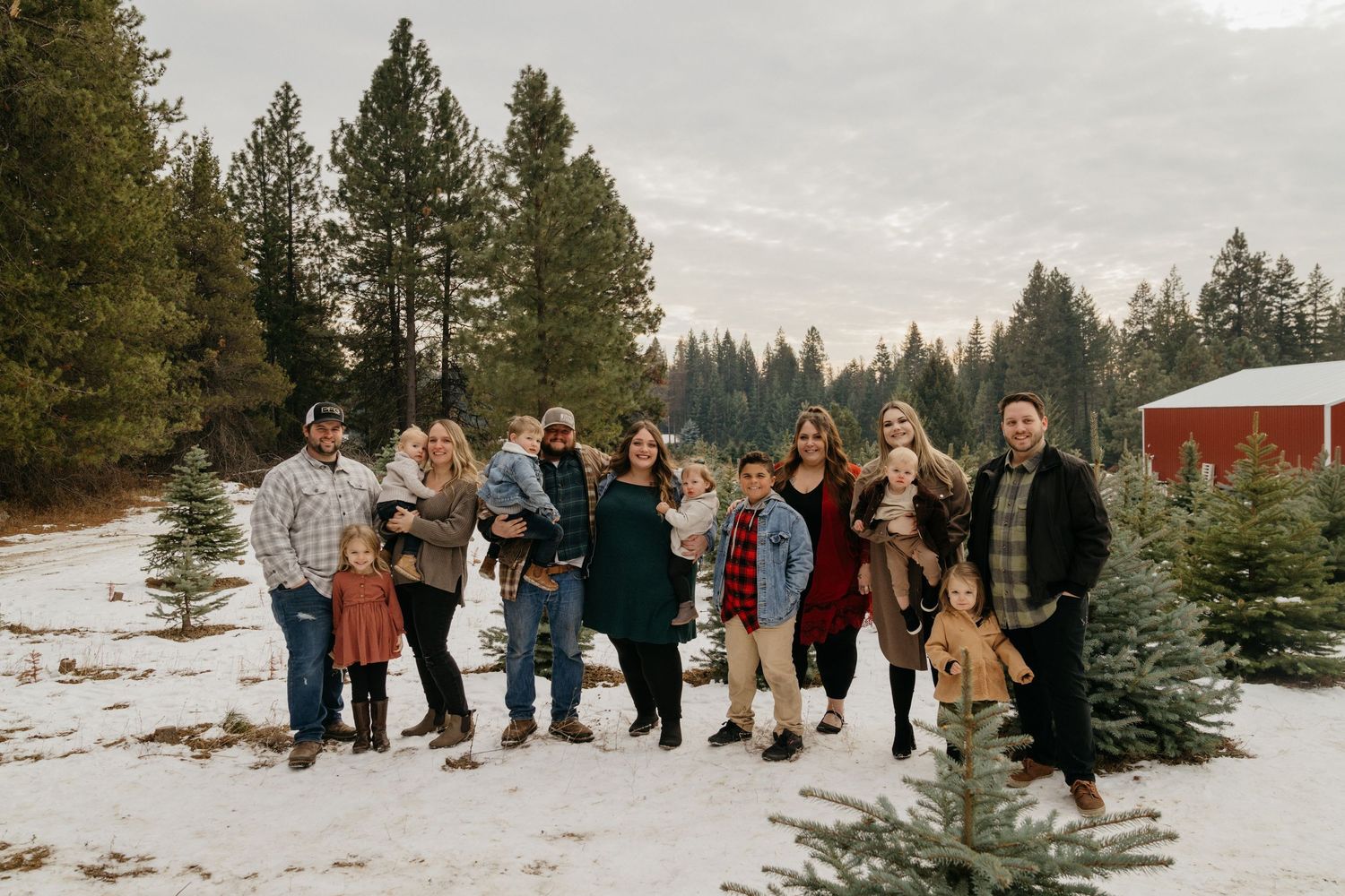 Group photo of people standing in snow near evergreen trees and red barn.