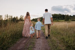Family walking together on a dirt path through a meadow at sunset.