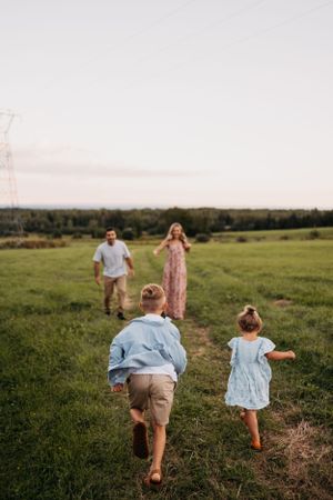 Family playing chase in a green field with power lines visible in the background.