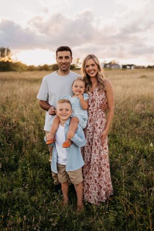 Sunset family photoshoot in a rustic field with tall grass and cloudy sky backdrop.