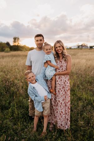 Family portrait in a golden field at sunset with parents and two children wearing coordinated outfits.
