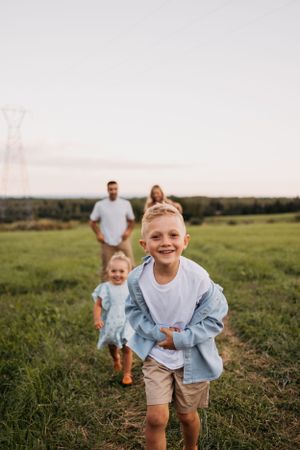 Children running joyfully through a grassy field with parents in the background.