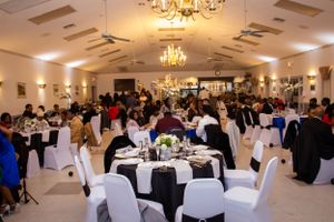 An elegant banquet hall setup with white chairs and tables under crystal chandeliers.