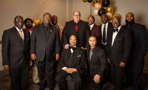 Group photo of men in formal suits posing together at an event.