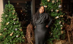 Elegant event setup with Christmas trees and holiday decorations along a wall.