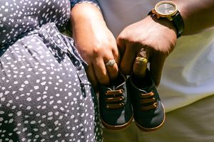 Hands holding small baby shoes against polka dot fabric.
