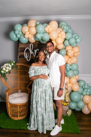 Couple poses under peach and mint balloon arch with peacock chair and floral decorations.