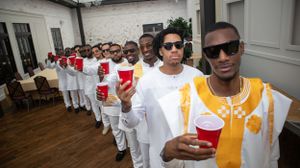 A line of attendees in white and gold attire pose during a formal celebration.