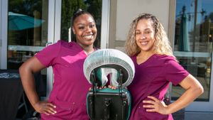 Two staff members in matching purple shirts pose with a stroller outside a storefront.