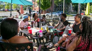 A group enjoys outdoor dining under green umbrellas at a casual restaurant patio.