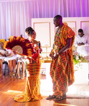 A couple in traditional African attire performs a ceremonial dance at an indoor celebration.