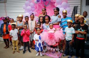 A large group of children and adults pose together in front of pink and purple balloon decorations.