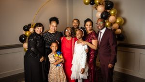 Family portrait of seven people in formal attire posing in front of gold and black balloons.