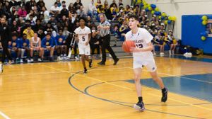 Basketball player dribbles down court during intense high school game with packed crowd watching.