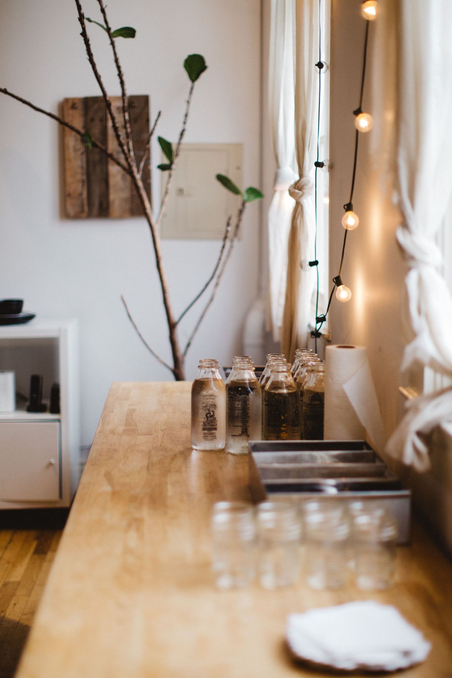 Rustic wooden table with glass jars and branches against white wall with string lights.